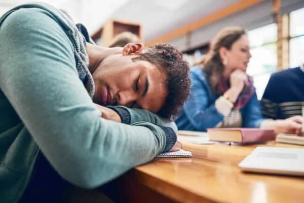 Stock image of student sleeping in class with his head down.