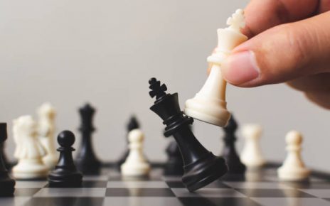 Stock image of a chess board with chess pieces and a hand moving one.