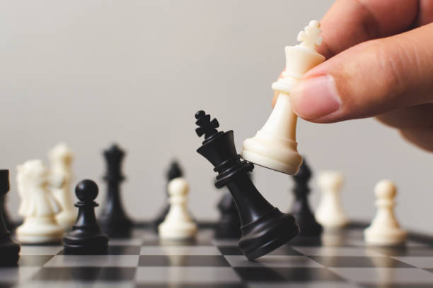Stock image of a chess board with chess pieces and a hand moving one.